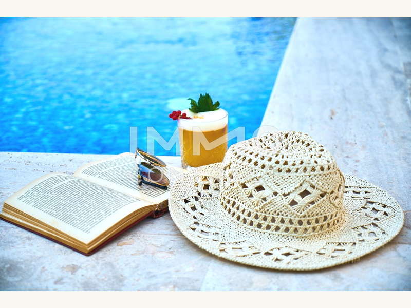 Symbolfoto Buch und Hut am Pool